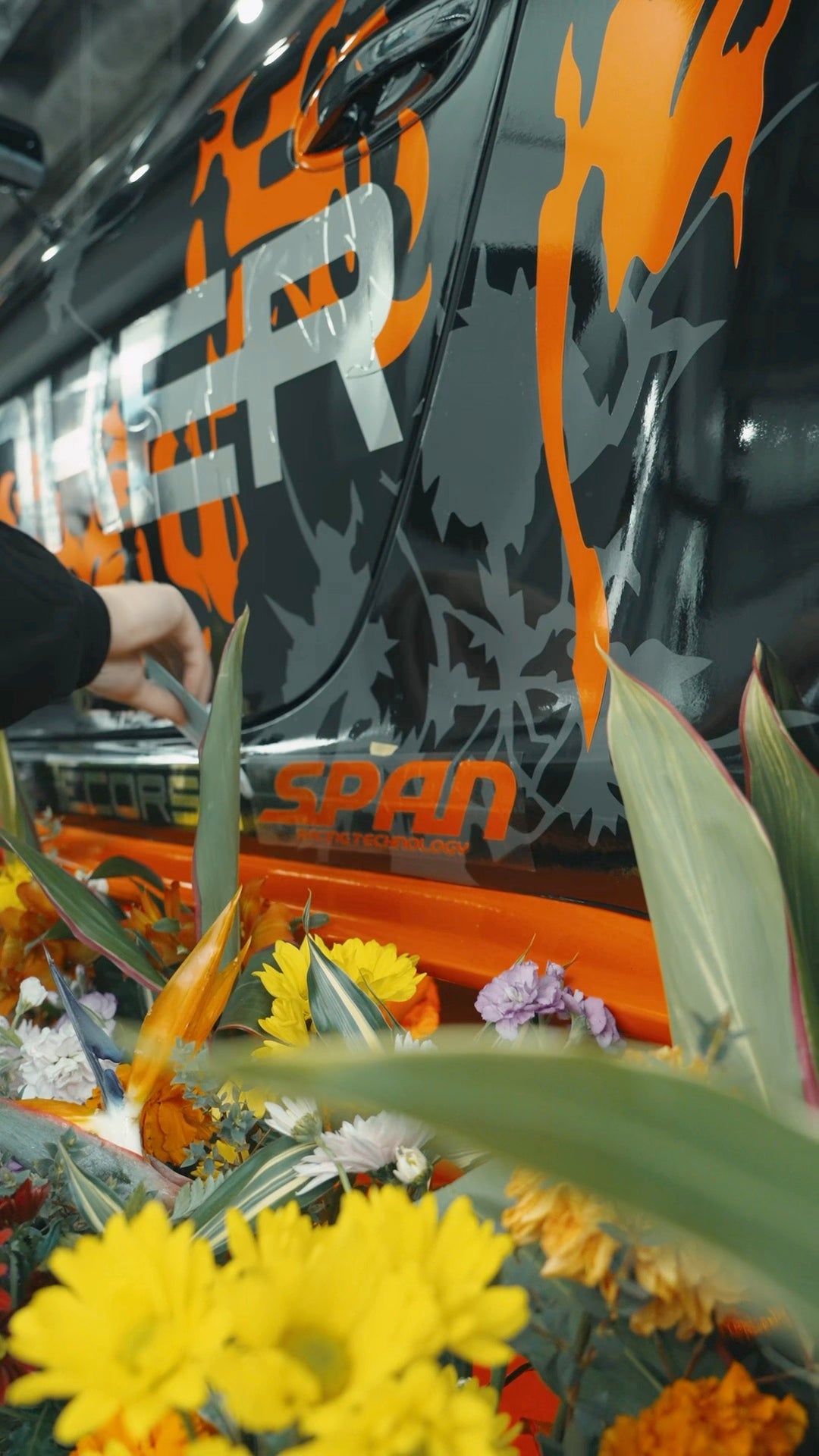 Flowers beside REVENANT’s orange and black artwork, from JOKER’s original ECHOES film